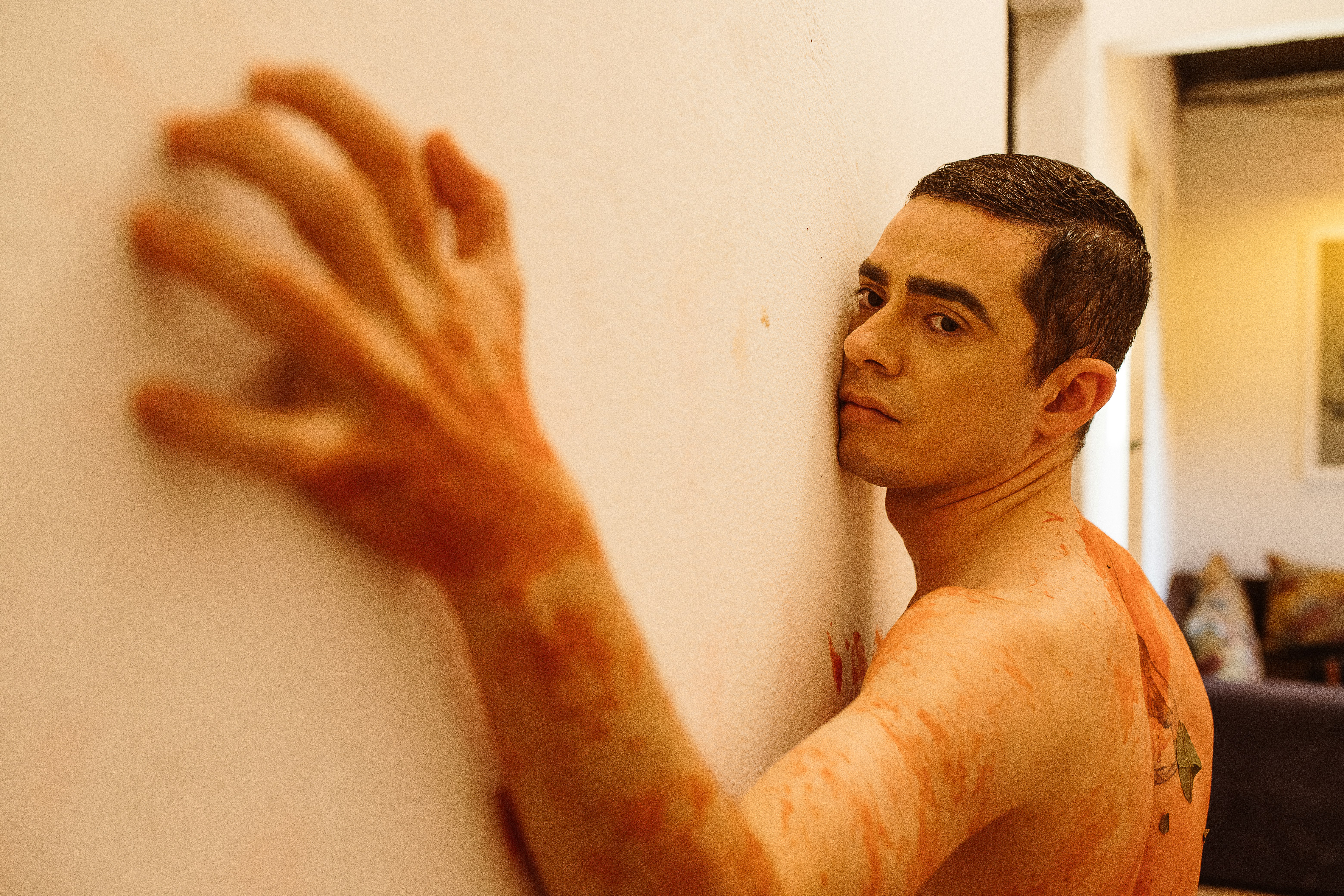 topless man leaning on white wall